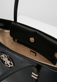 Czarna skórzana torba na ramię o teksturowanej powierzchni, z złotymi akcesoriami i zamknięciem na zamek. Wnętrze wykończone beżową podszewką i detalem z logo.