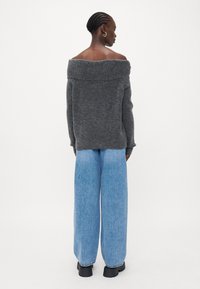 Grå av-shoulder genser med avslappet passform, paret med løse lyseblå jeans og svarte kraftige støvler. Glatt tekstur, minimal design.