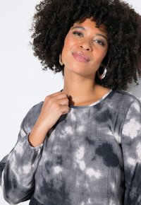 Langärmlig grijs-zwart tie-dye top met een ronde halslijn, textuurstof en gerimpelde mouwboorden, met een zachte, gladde afwerking.