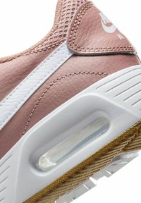 Zapatilla de piel rosa con acentos blancos, que presenta un diseño texturizado, panel de malla, almohadilla de aire visible y una suela de goma con surcos.