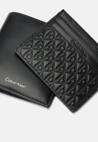 Juego de cartera y tarjetero de cuero negro, con un patrón geométrico texturizado y logo grabado. Superficie lisa con costuras en contraste.