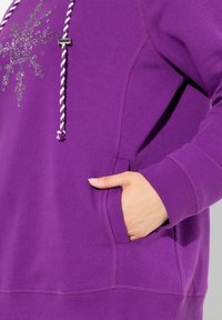 Felpa viola con design in strass argentati, cordino a fune e tasca a marsupio. Tessuto liscio, maniche a sbuffo e vestibilità rilassata.