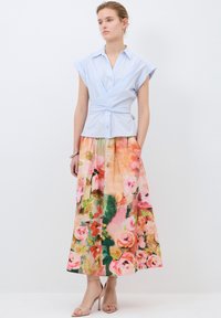 Vaaleansininen kietaisupaita, jossa on hihat, yhdistettynä pitkään kukkamekkoon, joka on koristeltu vaaleanpunaisilla ruusuilla ja vihreillä yksityiskohdilla; korkeat sandaalit viimeistelevät asun.