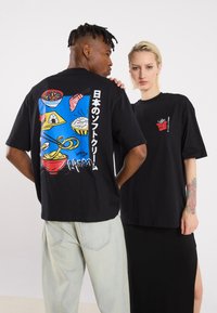 Sorte bomulds T-shirts med farverige madgrafikker på ryggen og små accenter på forsiden. Løs pasform med korte ærmer.
