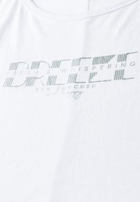 T-shirt en coton blanc avec un texte imprimé vert : "BREEZE FRESH & WHISPERING SUN TOUCHED and happy" avec des accents de ligne horizontale.