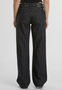 Jeans negros de tiro alto y pierna ancha con un tejido de mezclilla texturizado, que presentan dos bolsillos traseros y una etiqueta de cuero con marca en la cintura.