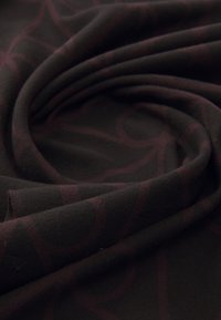 Mørkt stof med subtilt maroon geometrisk mønster, blødt foldet i en spiralform, der skaber et lagdelt texture og dybde.