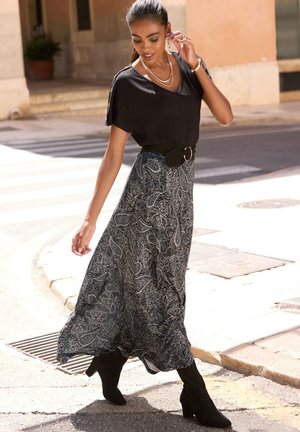 Schwarzes Kurzarmoberteil kombiniert mit einem langen, gemusterten Rock in Schwarz und Weiß. Accessoires: schwarzer Gürtel und kniehohe schwarze Stiefel.