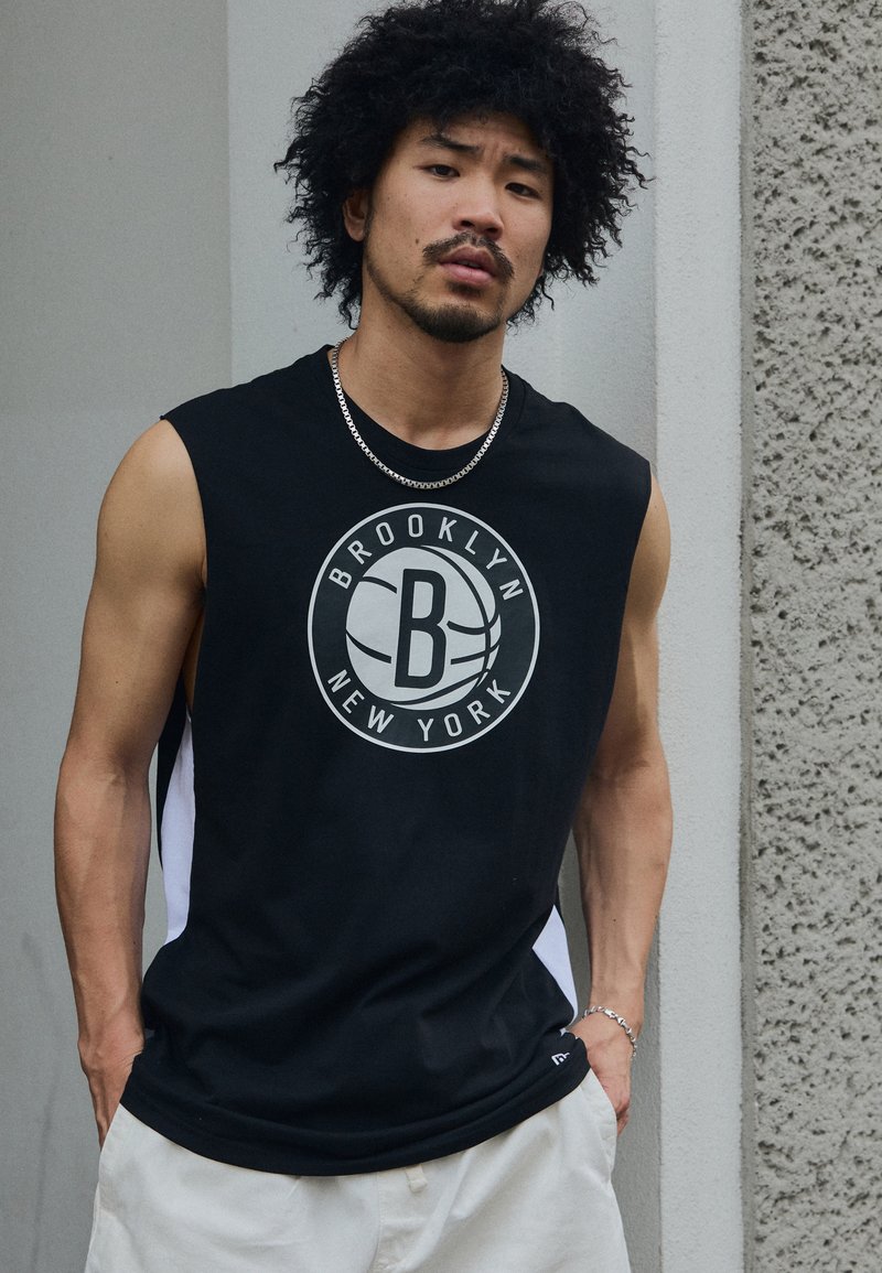 Camiseta atlética sin mangas de color negro con un gran logo circular de "Brooklyn New York", paneles laterales blancos y una textura de tela suave.