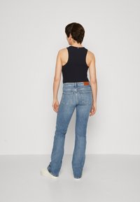 Canotta senza maniche di colore blu navy abbinata a jeans in denim azzurro a zampa. I jeans presentano tasche posteriori e un'etichetta in pelle marrone in vita.