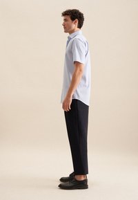 Camicia a maniche corte, blu e bianca a righe, con colletto, abbinata a pantaloni neri slim-fit e scarpe nere.