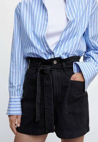 Koszula zapinana na guziki w niebiesko-białe paski, zestawiona z wysokim stanem czarnych jeansowych szortów z paskiem i przednimi kieszeniami.