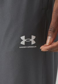 Sive kratke sportske hlače od teksturiranog materijala imaju bijeli Under Armour logo i prikazane su uz ruku koja prilagođava tkaninu.