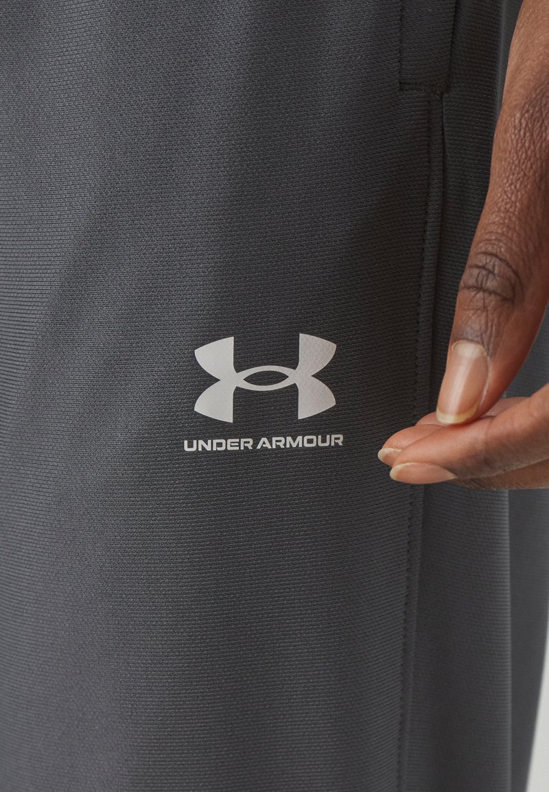 Pantalones cortos atléticos grises hechos de material texturizado con un logo blanco de Under Armour, mostrados junto a una mano ajustando la tela.