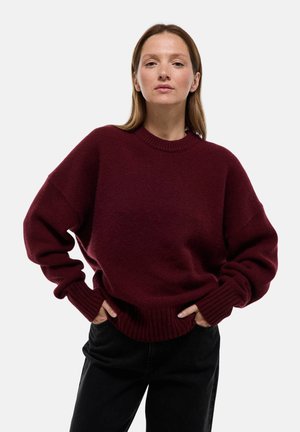 Pull en maille surdimensionné bordeaux avec un col rond, des poignets et un ourlet côtelés. Assorti avec un pantalon noir, créant une coupe décontractée.