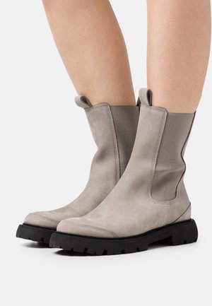 Grijze suède enkellaarzen met elastische zijpanelen en zwarte rubberen zolen. Voorzien van aantreklusjes voor eenvoudig aan- en uittrekken en een gestroomlijnd ontwerp.