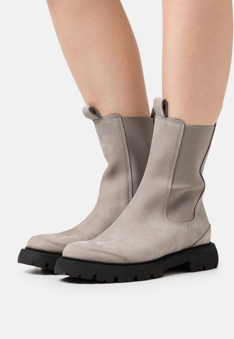 Bottes cheville en daim gris avec panneaux latéraux élastiques et semelles en caoutchouc noir. Dotées de languettes pour un enfilage facile et d'un design épuré.