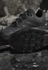 Chaussures de randonnée noires sur un sol rocheux, mettant l'accent sur la semelle texturée avec des crampons profonds pour l'adhérence en extérieur et une tige imperméable.