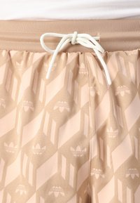 Béžové sportovní šortky s opakujícím se vzorem loga, elastickým pasem se šňůrkou a hladkou, lehkou tkaninou.