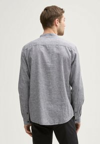 Chemise grise à manches longues en tissu texturé, avec des poignets à boutons et un col classique. La vue arrière montre un ourlet arrondi et des détails de couture minimaux.
