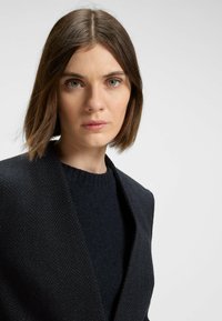 Sort jakke med fiskebensmønster og sjalskrave, parret med en mørkeblå crewneck sweater. Glat tekstur og skræddersyet pasform.