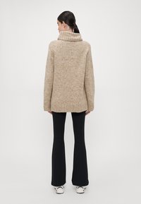 Beige gebreide trui met een col, losse pasvorm, geribbelde onderrand en lange mouwen, gecombineerd met zwarte flarebroek en witte sneakers.