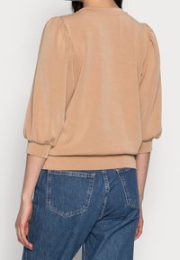 Top de punto beige con mangas abullonadas, tejido suave, puños de canalé y dobladillo. Combinado con vaqueros de mezclilla azul de cintura alta con bolsillos traseros.