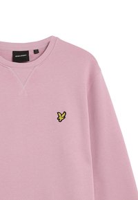 Sudadera rosa con cuello redondo, puños acanalados y un pequeño logotipo bordado en negro y amarillo en el lado izquierdo del pecho. Textura de tela suave.