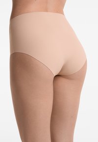 Beige högmidjade trosor tillverkade av ett smidigt och stretchigt tyg. Har full täckning utan synliga sömmar, vilket ger ett sömlöst utseende.