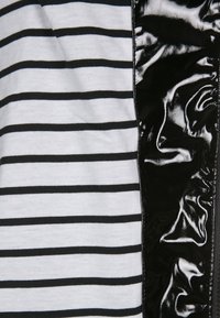 Mustavalkoraidallinen kangas toisella puolella, kiiltävää mustaa patenttimateriaalia toisella; kontrastoivia tekstuureja ja kuvioita.