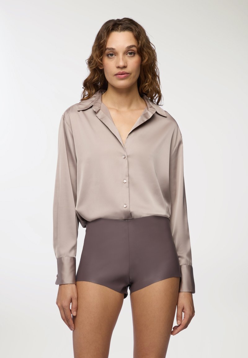 Blusa in satin a maniche lunghe color taupe chiaro con colletto e chiusura a bottoni, abbinata a pantaloni corti a vita alta color marrone scuro con una texture liscia.
