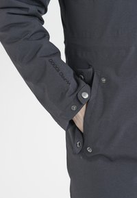 Veste noire imperméable avec un tissu texturé, fermeture à boutons-pression, poche latérale et étiquette "WR 10000" sur la manche.