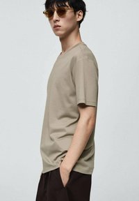T-shirt beige a maniche corte con scollatura tonda, realizzata in tessuto morbido, abbinata a pantaloni marroni e completata con occhiali da sole marroni.
