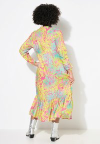 Abito a maniche lunghe in un vivace motivo astratto rosa, giallo e verde. Presenta un orlo a strati e una vestibilità comoda. Stivaletti argento alla caviglia completano il look.