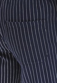 Granatowy materiał w białe prążki, z tylną kieszenią, teksturowanym wykończeniem, dopasowanym krojem i starannym przeszyciem.