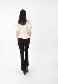 Top corto de color beige claro, de manga corta y ajuste holgado, combinado con pantalones negros acampanados y botas negras de tacón grueso, visto desde la parte de atrás.