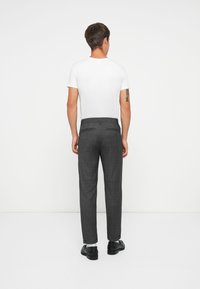 Grau gemusterte Hose mit taillierter Passform, ausgestattet mit Gesäßtaschen und einem Bund, kombiniert mit einem schlichten weißen T-Shirt und schwarzen Schuhen.