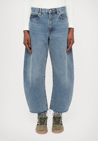 Jeans en denim bleu clair avec une coupe ample, dotés d'une taille haute, d'ourlets effilochés et de cinq poches. Associés à des baskets vert olive.
