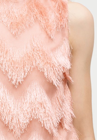 Μπλούζα χωρίς μανίκια σε ροζ απόχρωση με υφασμένα, τριγωνικά διακοσμητικά σχέδια στο πάνω μέρος του κορμού ενός ατόμου και εμφανές γυμνό χέρι.