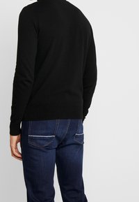 Svart stickad tröja med långa ärmar och ribbad nederkant, tillsammans med mörkblå denimjeans med kontrastsömmar på fickorna.