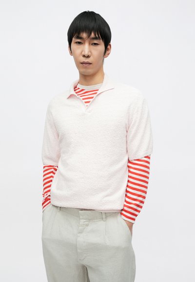 Ροζ ανοιχτόχρωμο φλις πάνω μέρος με γιακά, φορεμένο πάνω από κόκκινο και λευκό ριγέ πουκάμισο με μακριά μανίκια. Ανοιχτό γκρι παντελόνι με άνετη εφαρμογή.