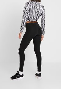 Donna che indossa leggings neri con il logo Adidas a righe bianche lungo il lato, una maglietta a maniche lunghe bianco e nera con logo Adidas, e sneakers nere.