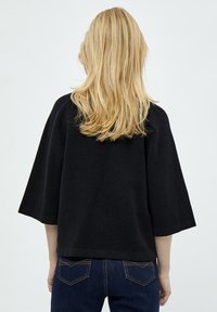 Maglione nero, oversize, con maniche ampie e taglio squadrato, realizzato in un materiale morbido. Abbinato a jeans scuri, presenta un design semplice.