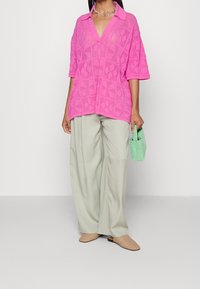 Rosa kortärmad stickad topp med krage och en strukturerad diamantmönster, kombinerad med ljusgröna vida byxor och en liten grön handväska.