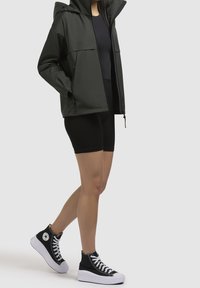 Mörkgrön hoodie-jacka, svart åtsittande topp och svarta cykelshorts. Bärs med svarta högklackade sneakers med vit sula och snörning.