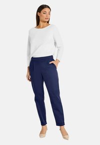 Witte lange mouwen trui, ontspannen pasvorm. Marineblauwe tapered broek met zijzakken. Model draagt beige hoge hakken. Schoon, minimalistisch ontwerp.