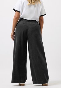  levelegged mustat farkut korkealla vyötäröllä, kahdella takataskulla ja reilulla istuvuudella, yhdistettynä tiukkaan valkoiseen t-paitaan, jonka reunat ovat mustat.