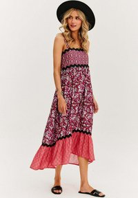 Sukienka maxi w kolorze burgundowym, zwiewna, z wzorzystą górą i kontrastującą dolną częścią w różowe kwiaty, z czarną koronkową lamówką przy talii.