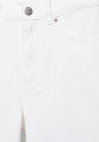 Nærbillede af hvide denimjeans, der viser linning, knap, bæltestrop og forlomme med nitte detaljer.