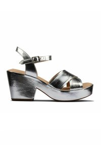 Metallisk sølv højhælet sandal med krydsede stropper, en ankelrem og en tyk kilehæl. Glat tekstur med en reflekterende finish.